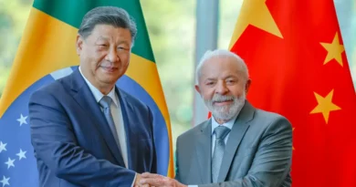 Lula e outro homem de terno apertam as mãos diante das bandeiras do Brasil e da China após anúncio de isenção de visto.