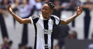 Jogador do Corinthians sorri com braços abertos no campo; torcida desfocada ao fundo em estádio de Londres.