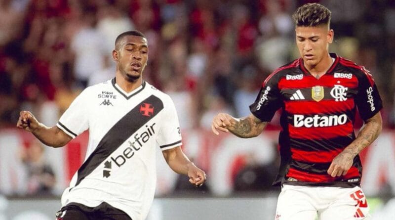 Jogador do Vasco disputa bola com atleta do Flamengo em campo, torcida ao fundo. Flamengo vence o clássico.