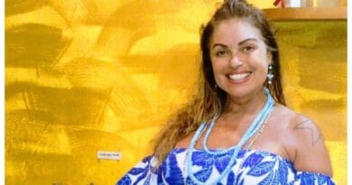 Mulher de cabelos castanhos sorri, usa vestido azul e branco e colar. Fundo amarelo destaca manchete sobre injúria racial.