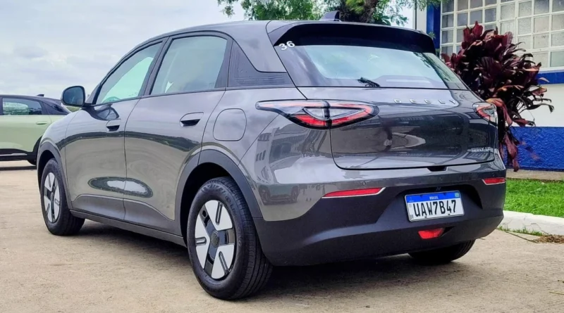 Carro elétrico Geely EX2 cinza com placa brasileira estacionado próximo a um prédio azul e branco, com luzes traseiras arredondadas.