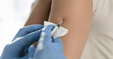 Profissional com luvas azuis aplica vacina contra câncer de pele no braço de paciente, segurando o olhar sobre a pele.